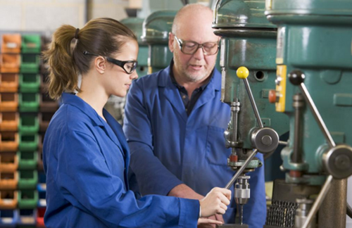 Female Student And Male Teacher Using Pillar Drill